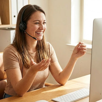 Woman in a customer support role at a desk with a computer, wearing a headset and smiling.