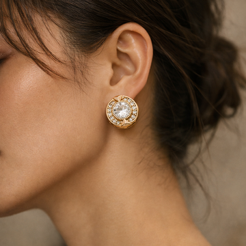 Close-up of a person wearing a gold earring with a clear gemstone.
